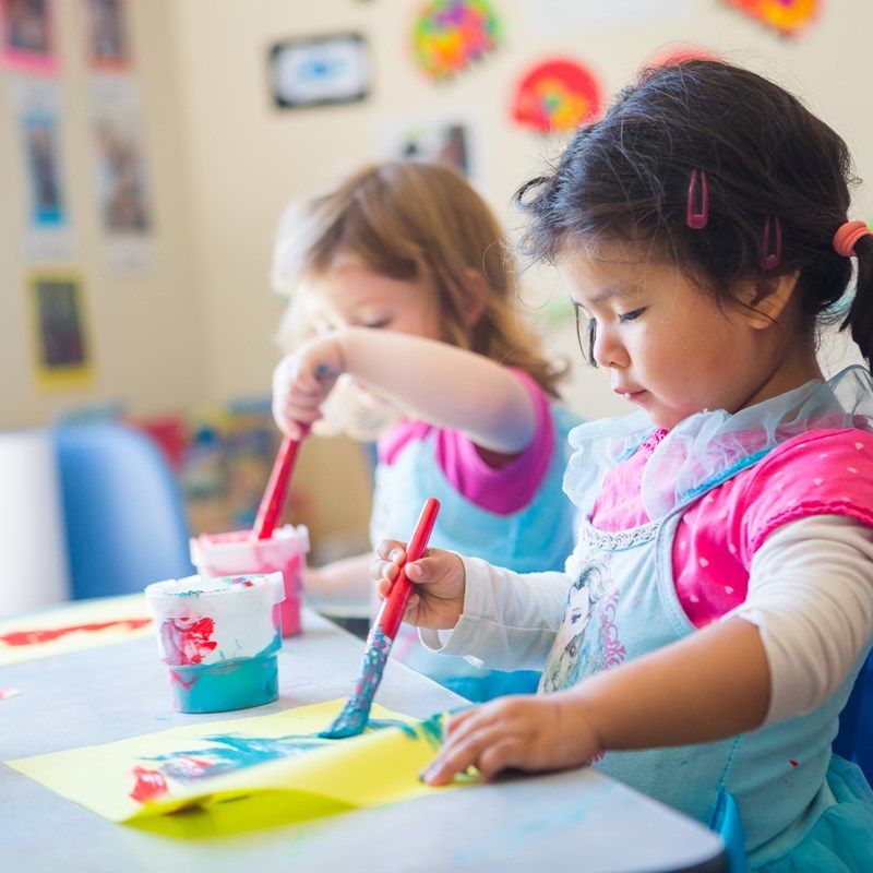 Two girls painting side by side at the art table