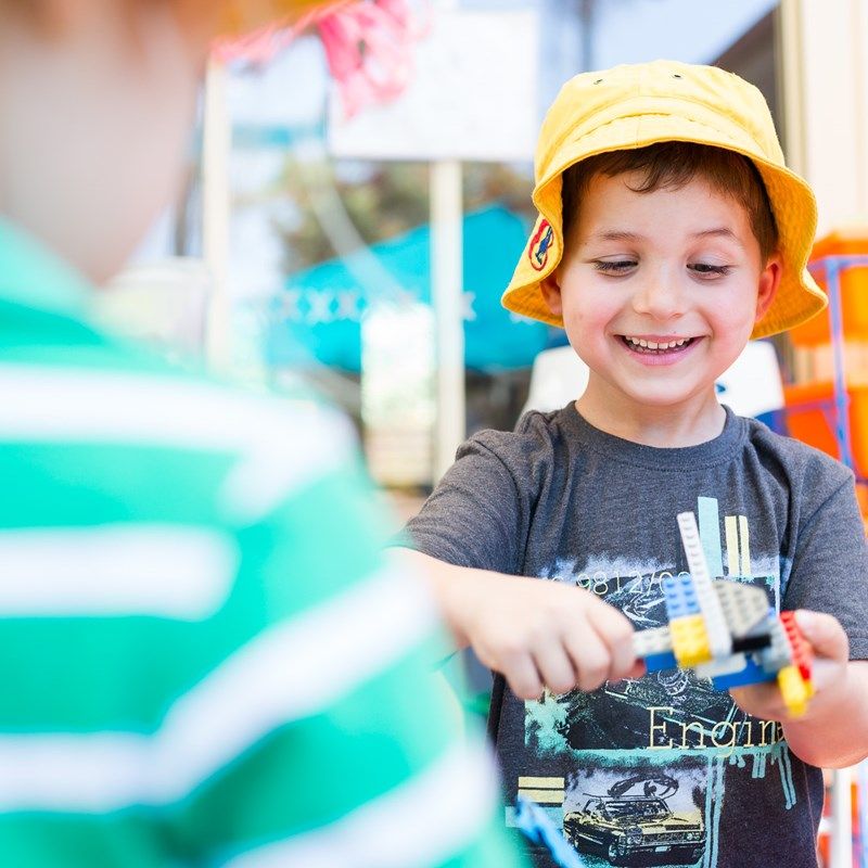 A boy in a sun hat proudly holding up a toy he built