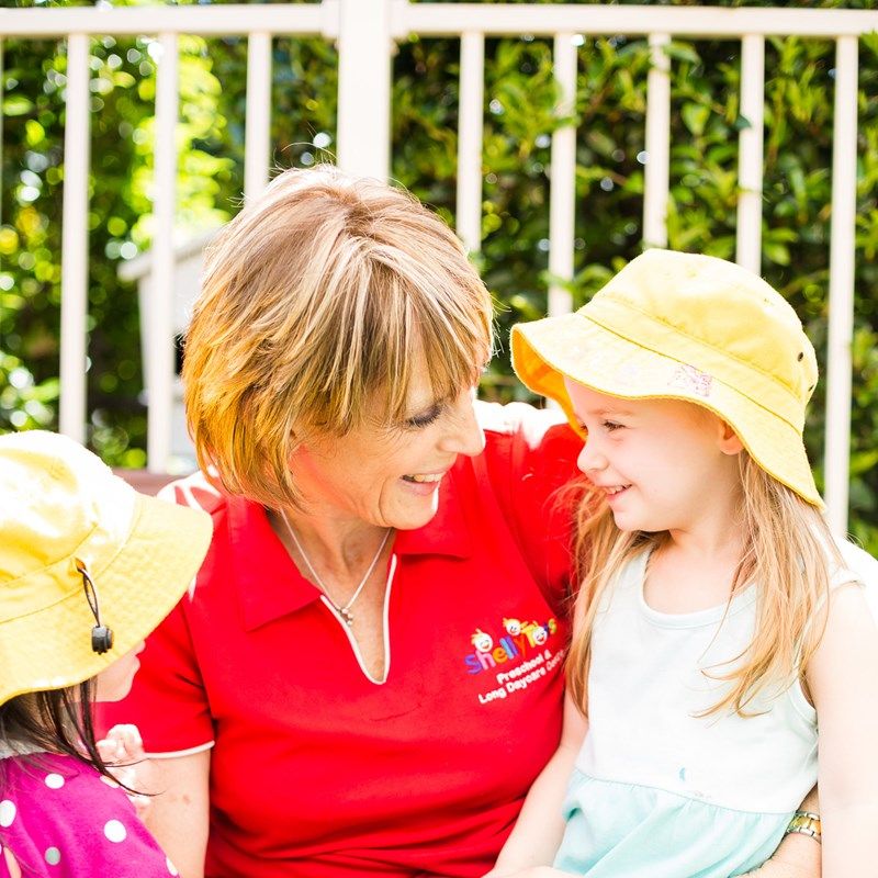 A ShellyTots educator sharing a smile with a girl in a yellow sun hat