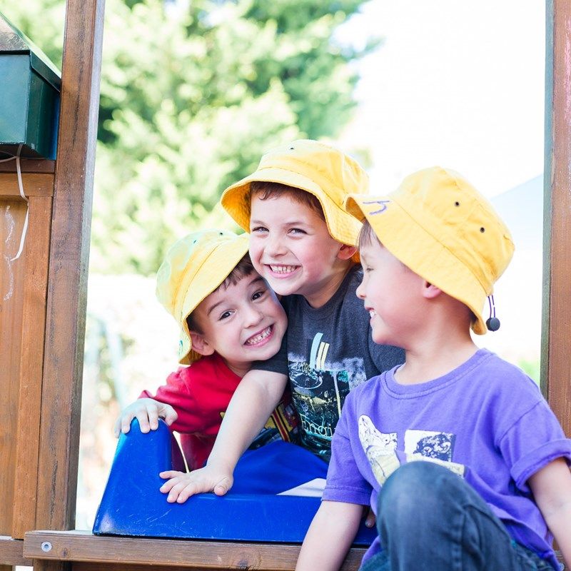 Three boys in sun hats laughing together on the playground