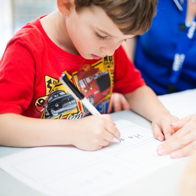 A boy carefully writing letters during a pre-literacy activity
