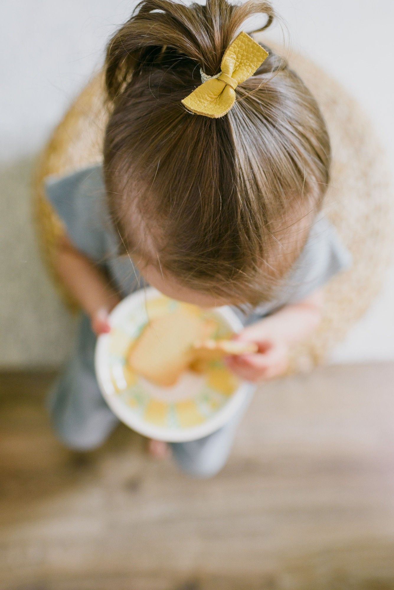 A toddler with a yellow hair bow enjoying a snack from a plate