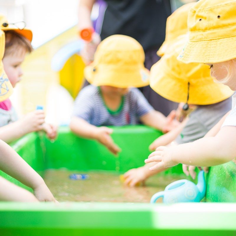 Toddlers in yellow sun hats splashing at a water play tray